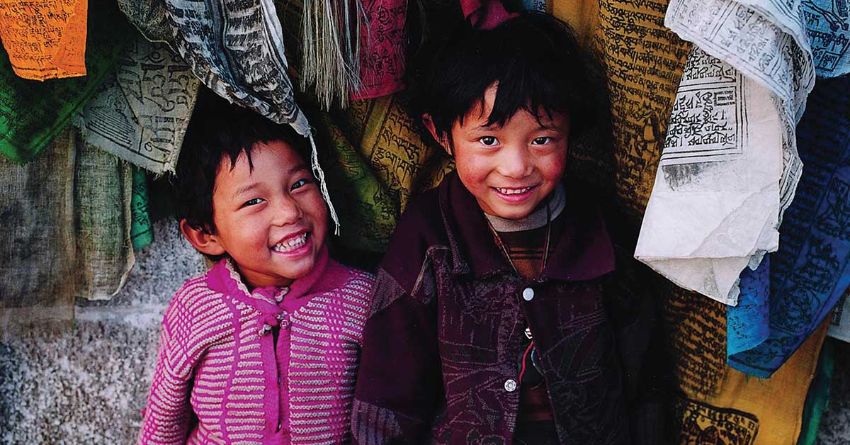 Two boys in Tibet (China) with prayer flags - by Jon Kaplan.